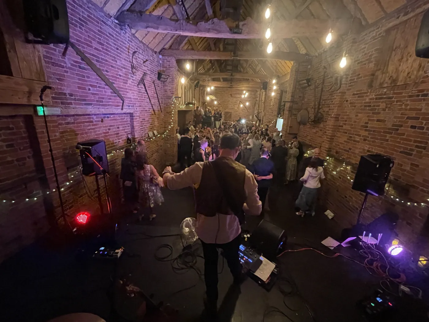 The band performing to a full dancefloor inside a rustic brick barn lit with festoon lights