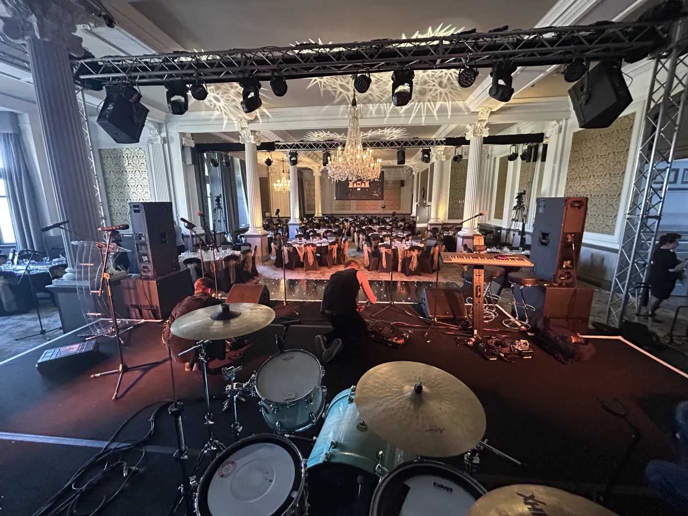 The band's stage and drum kit set up in an elegant chandelier-lit ballroom