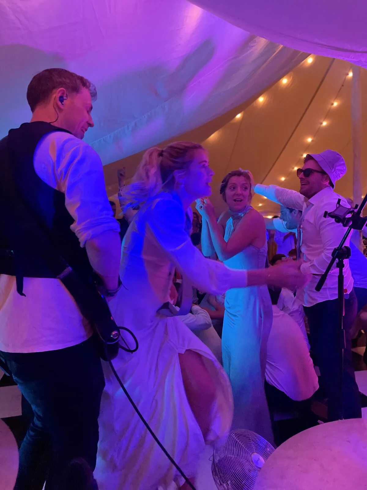 Lead singer with a bride dancing at the front of the dancefloor under purple and blue stage lights