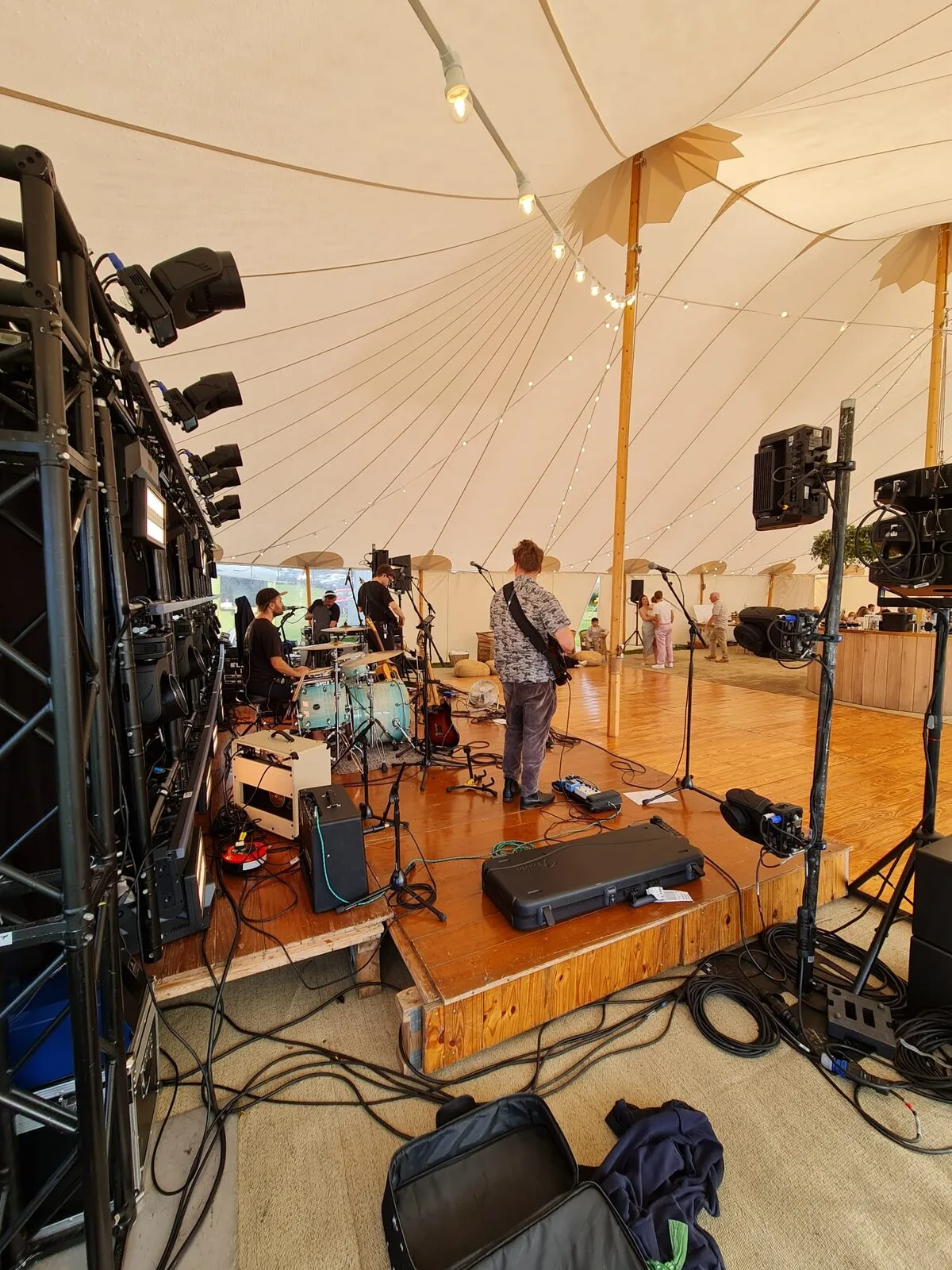 Band soundcheck on stage inside a sperry tent, drums and lighting rig visible
