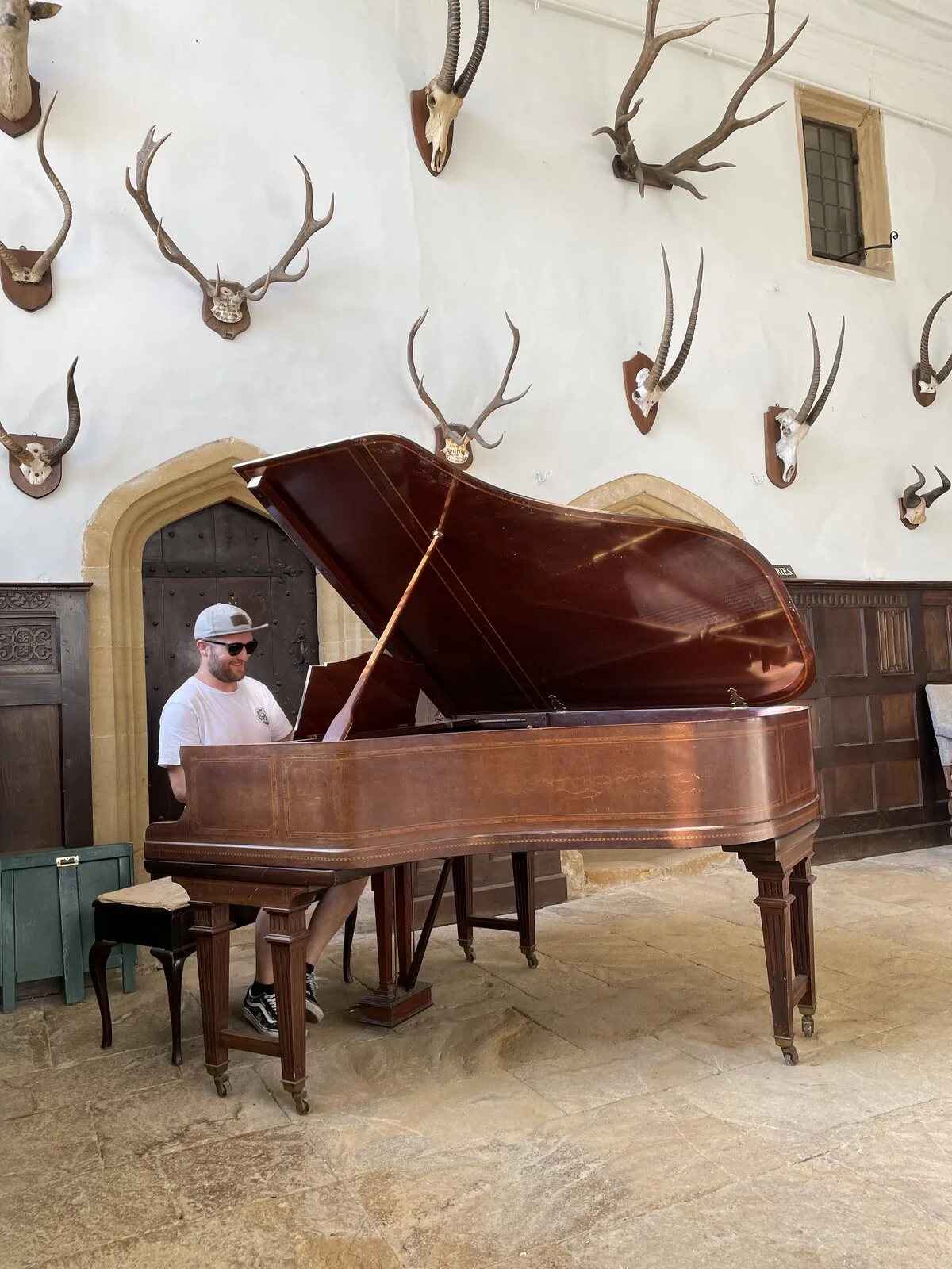 A band member playing a grand piano in a stone hall hung with antlers