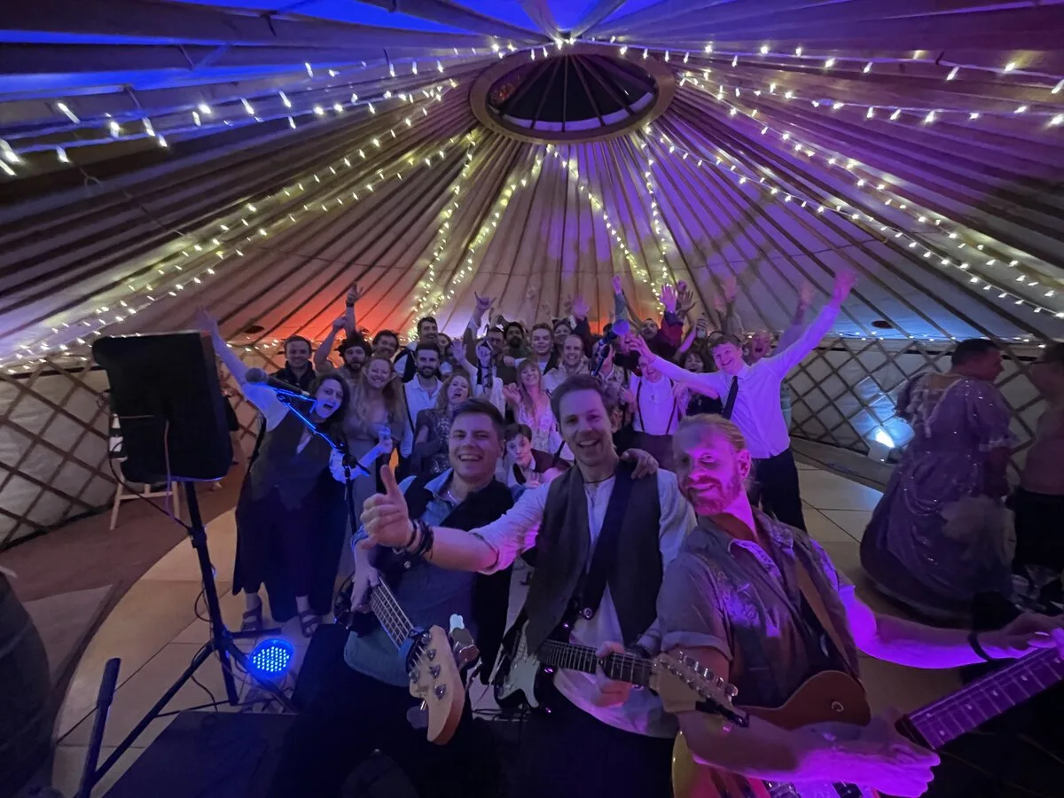 Band and wedding guests celebrating together on the dancefloor inside a fairy-lit yurt
