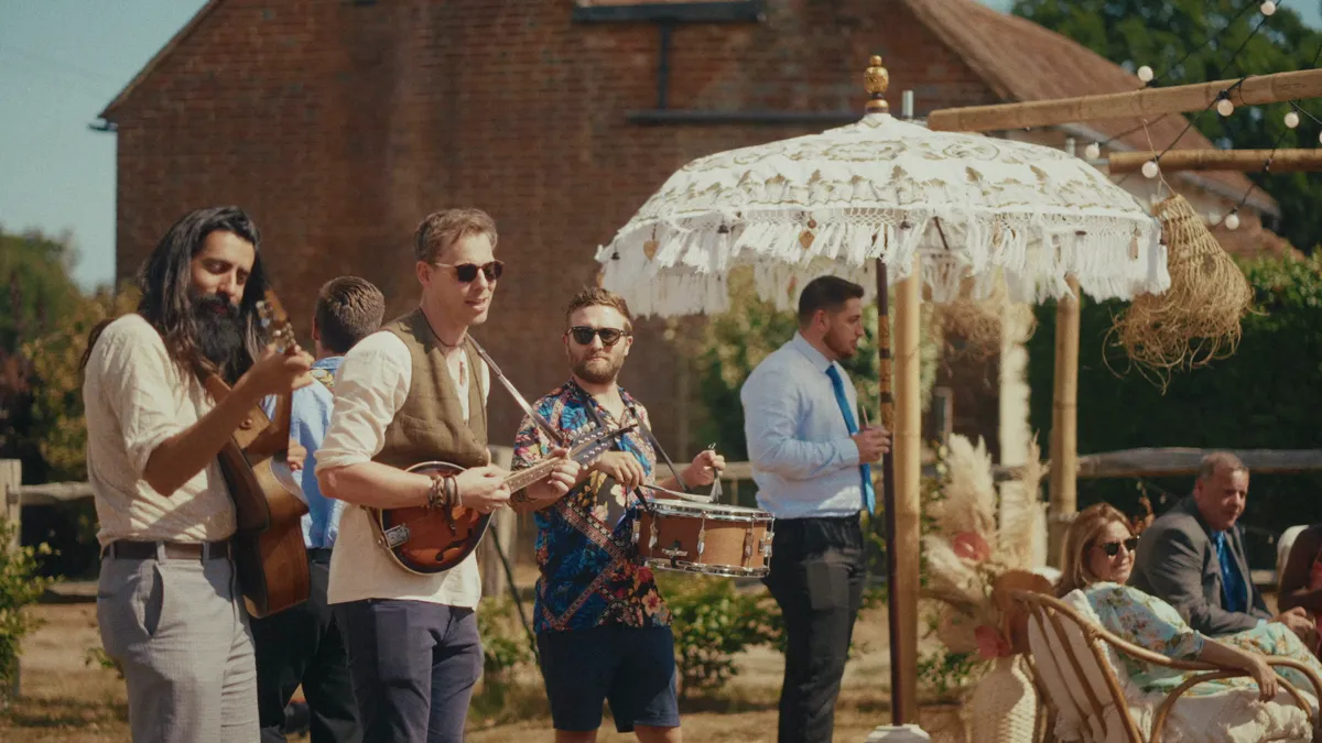 Kinmara playing among seated wedding guests in a garden, with the couple walking past behind them