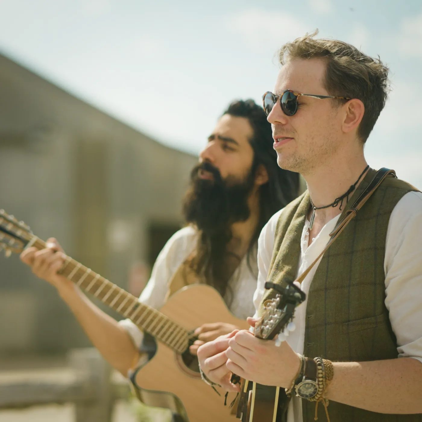 Two Kinmara musicians singing and playing acoustic guitar outdoors in the sun