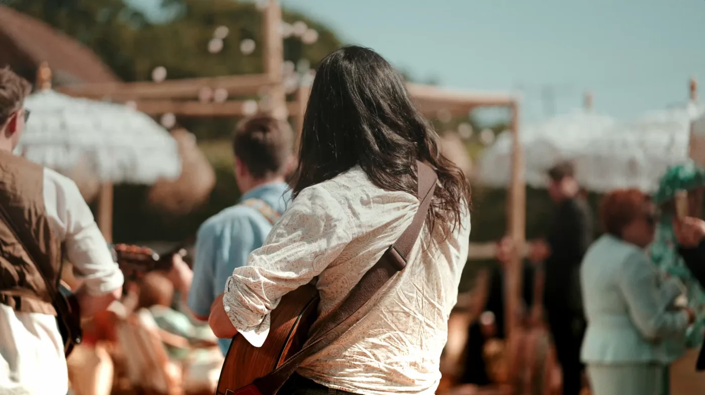 A guitarist playing to seated guests under parasols at a daytime wedding
